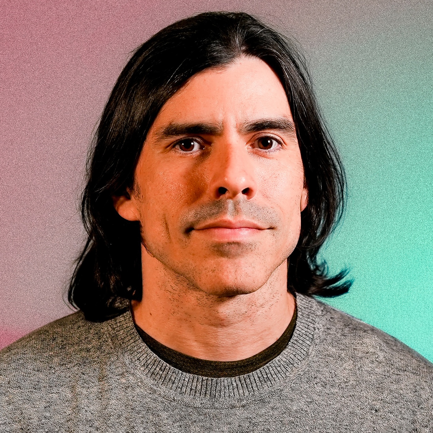 Juan Arzola's profile picture. He has long, black hair, is wearing a baseball style shirt and is looking towards the camera.